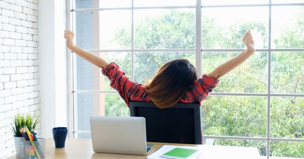 woman in office chair stretching her arms while looking outside through a large window